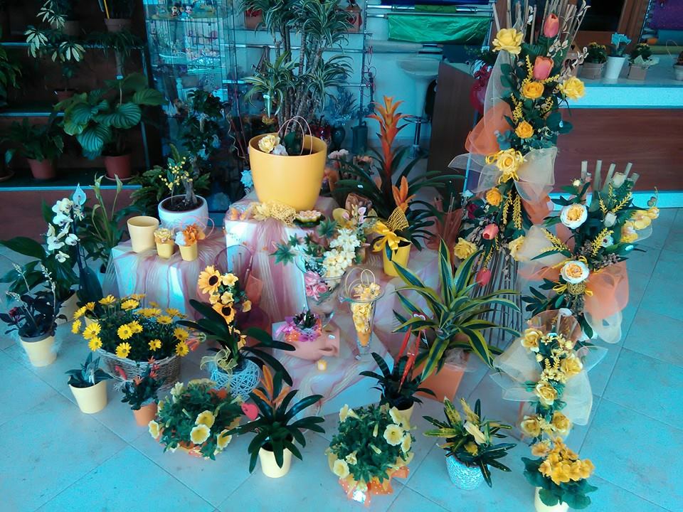 Esposizione di fiori in vaso e composizioni floreali, per lo più gialli e arancioni, in un ambiente da negozio.