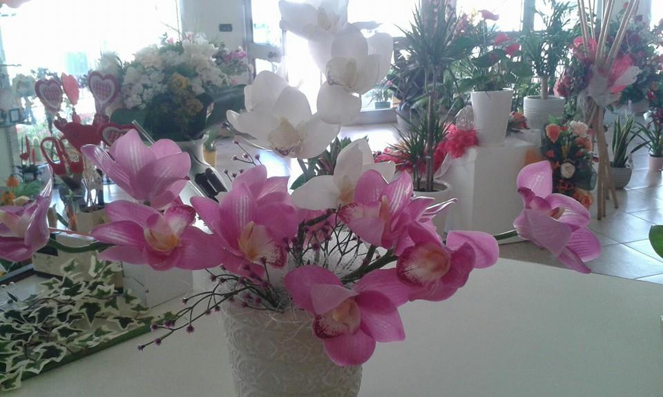 Orchidee rosa e bianche in un vaso bianco testurizzato, altri fiori e piante in un negozio.