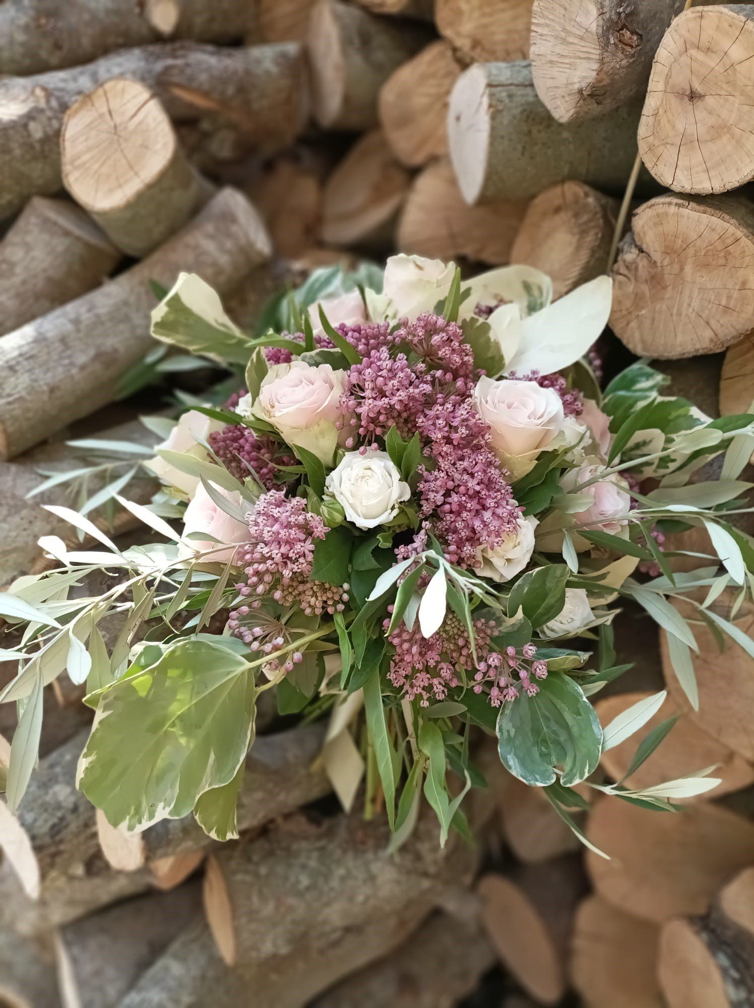 Bouquet di rose rosa e bianche, bacche viola e verde su una catasta di legna.