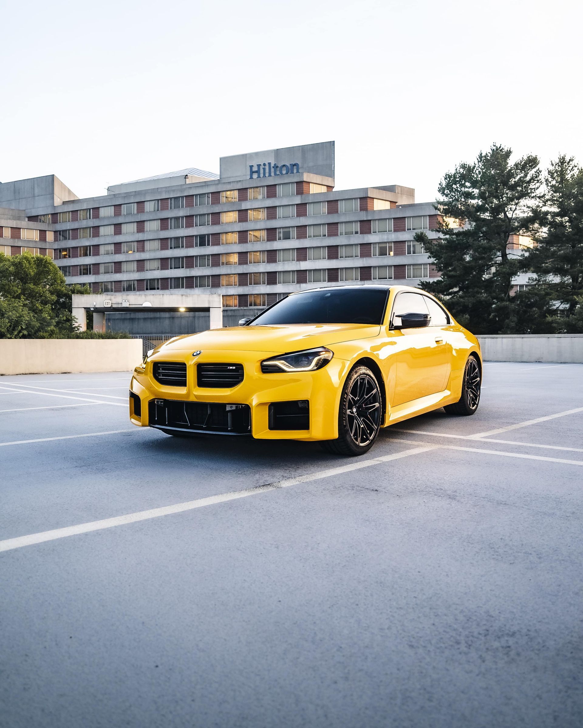 Yellow BMW M2 parked in front of a Hilton hotel.