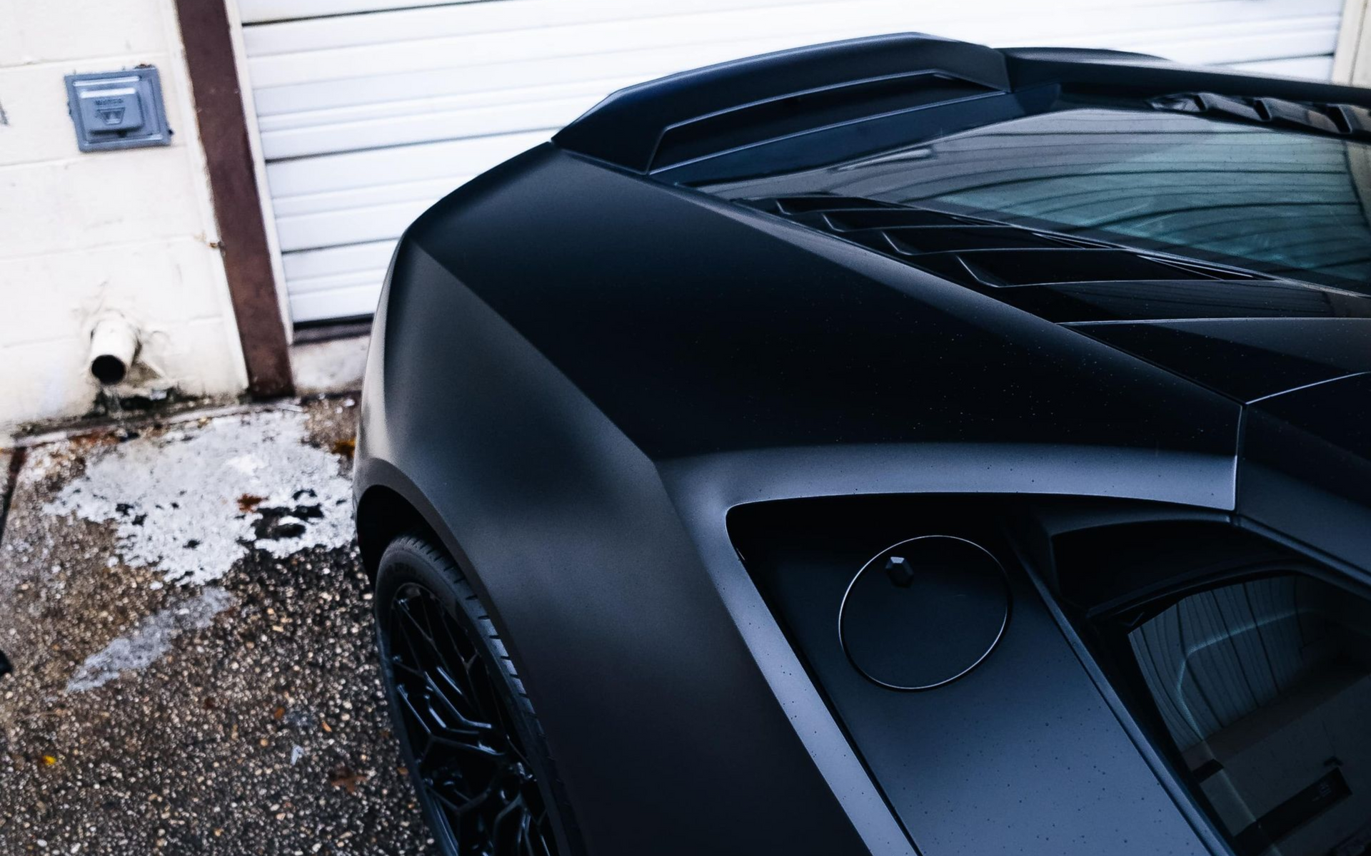 Black sports car parked near a garage with a matte finish.