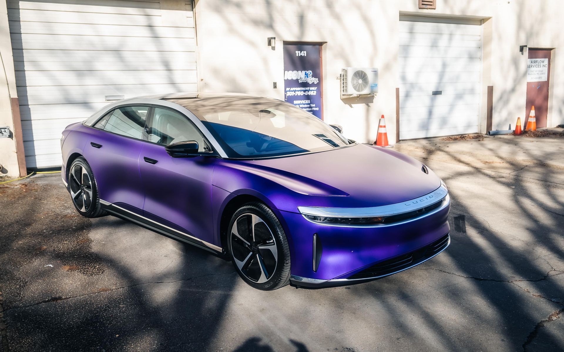 Purple electric car parked in front of garage doors, sunny day.
