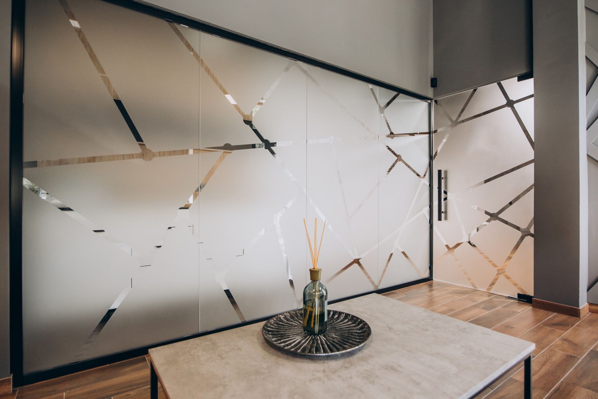Frosted glass wall with geometric design, small table with a decorative tray and diffuser.