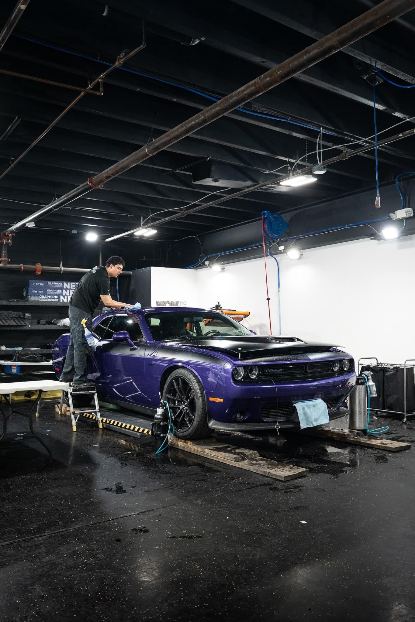 A person washes a purple Dodge Challenger inside a car detailing shop.