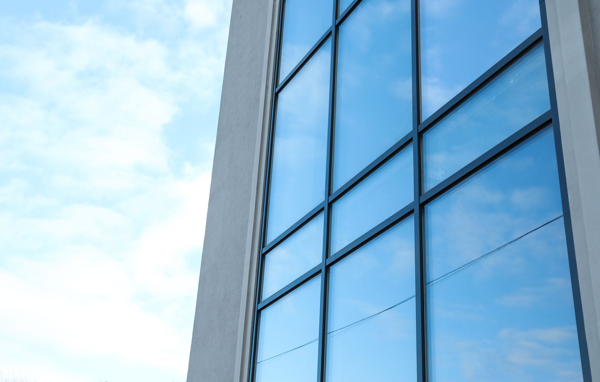 Tall building with reflective blue glass windows against a light blue sky.