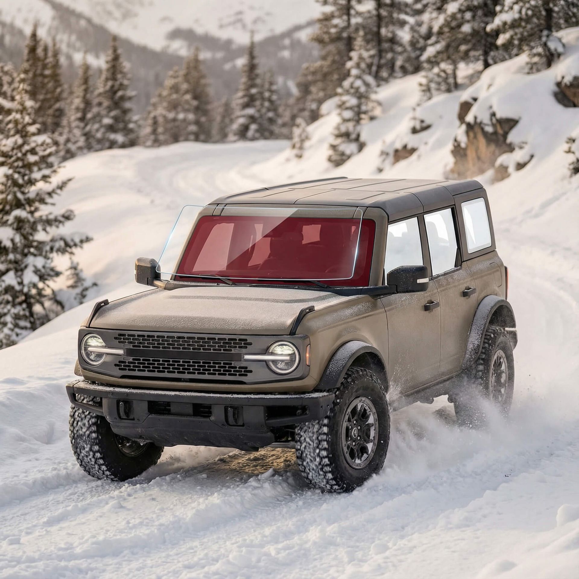 Ford Bronco SUV driving on a snowy mountain road, spraying snow.