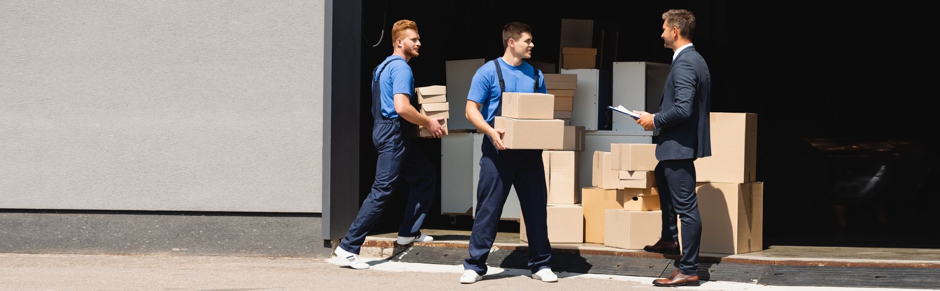 movers holding cardboard boxes near businessman with clipboard.