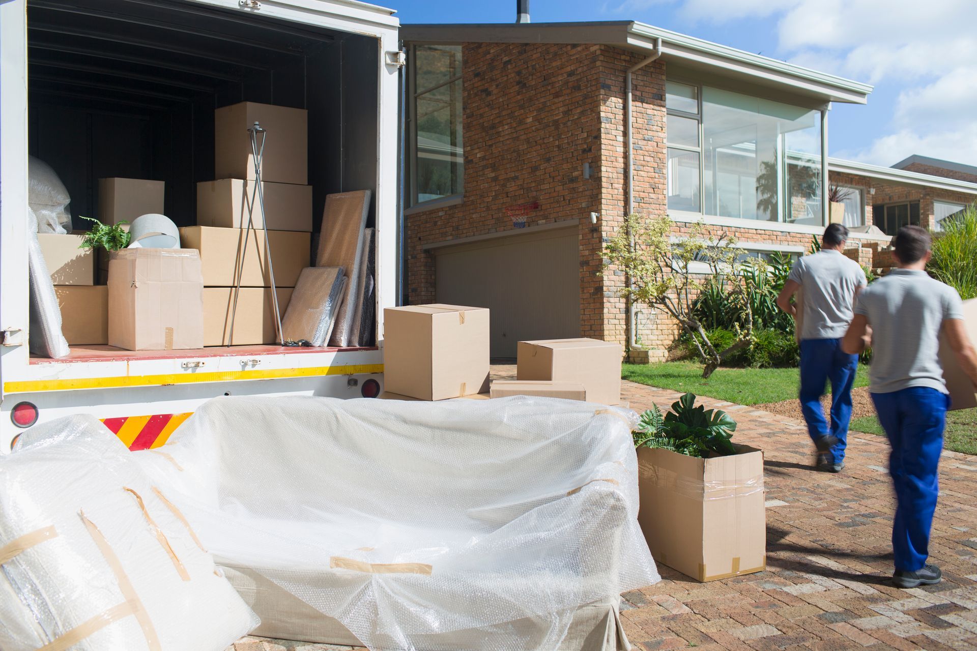 Moving truck with boxes and wrapped furniture outside a brick house.