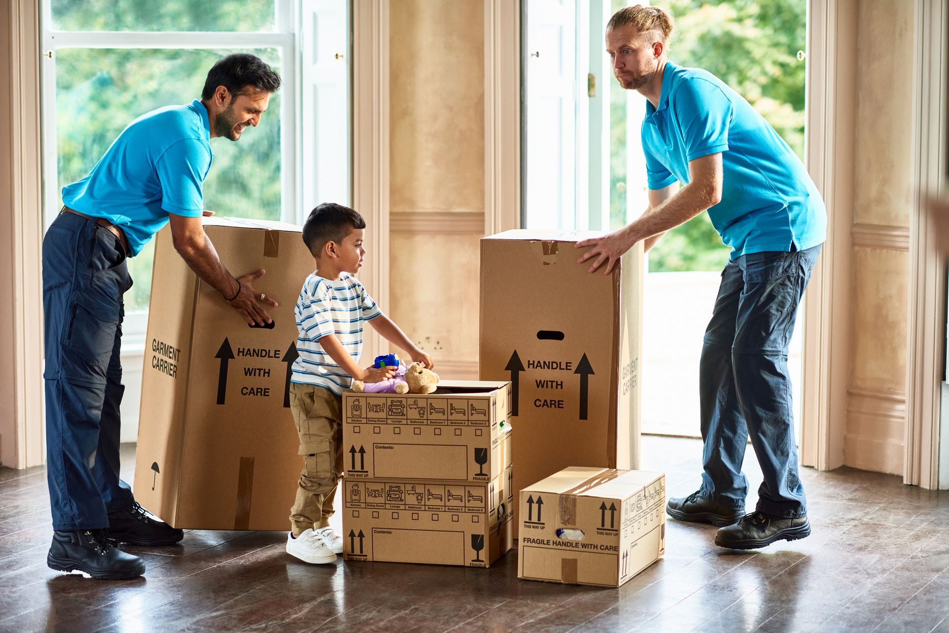 Removals men carrying boxes into empty room of new house with boy playing.