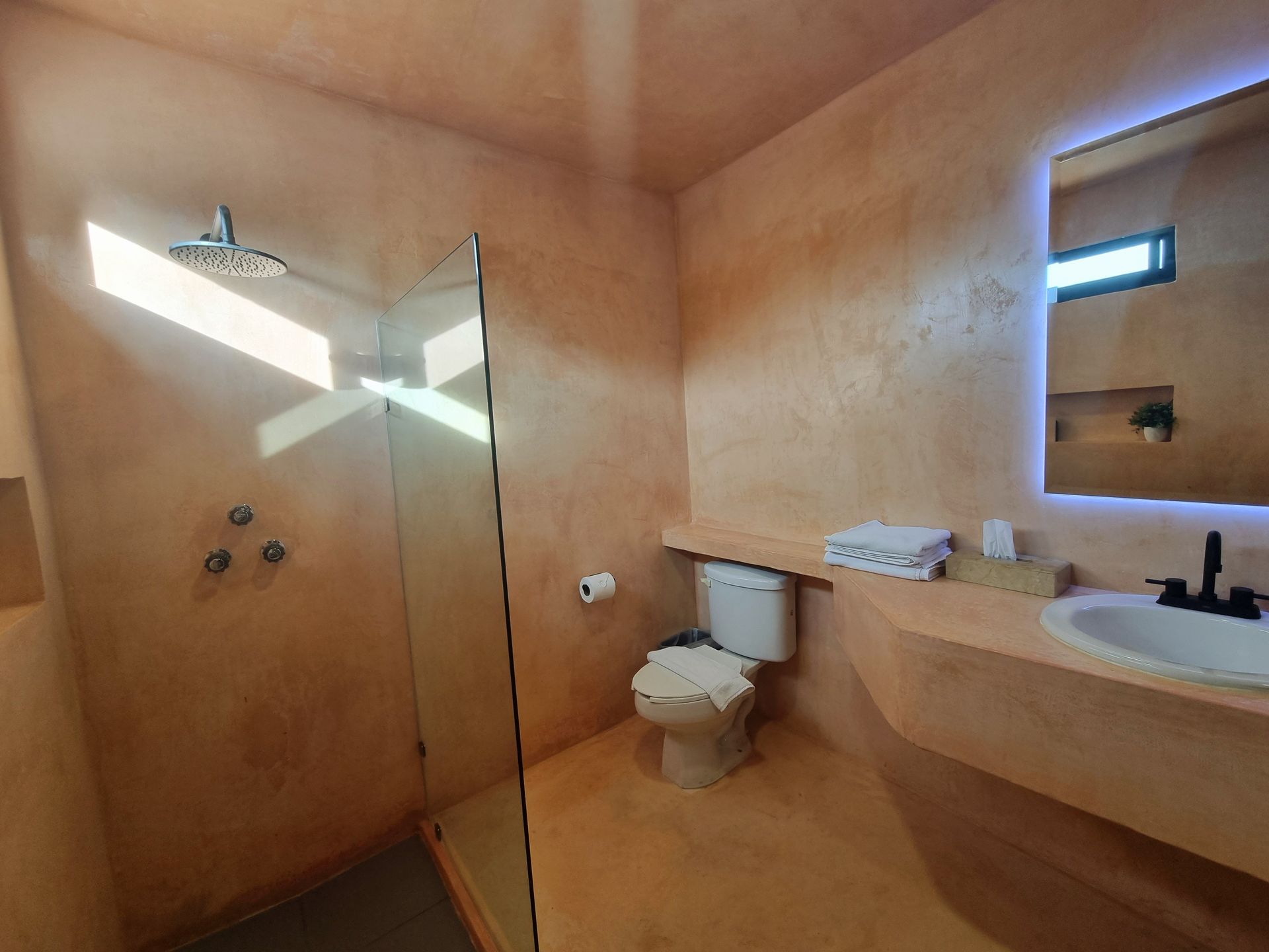 Un baño con inodoro, lavabo, ducha y espejo.