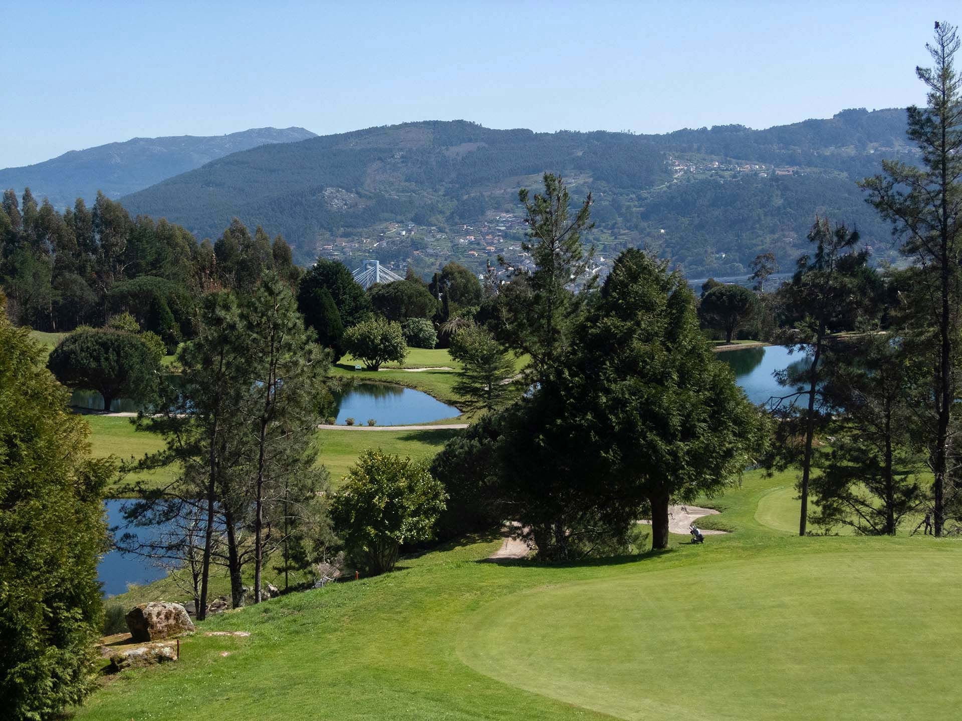 Golfplatz mit grünen Fairways, Bäumen, Teichen und Bergen im Hintergrund