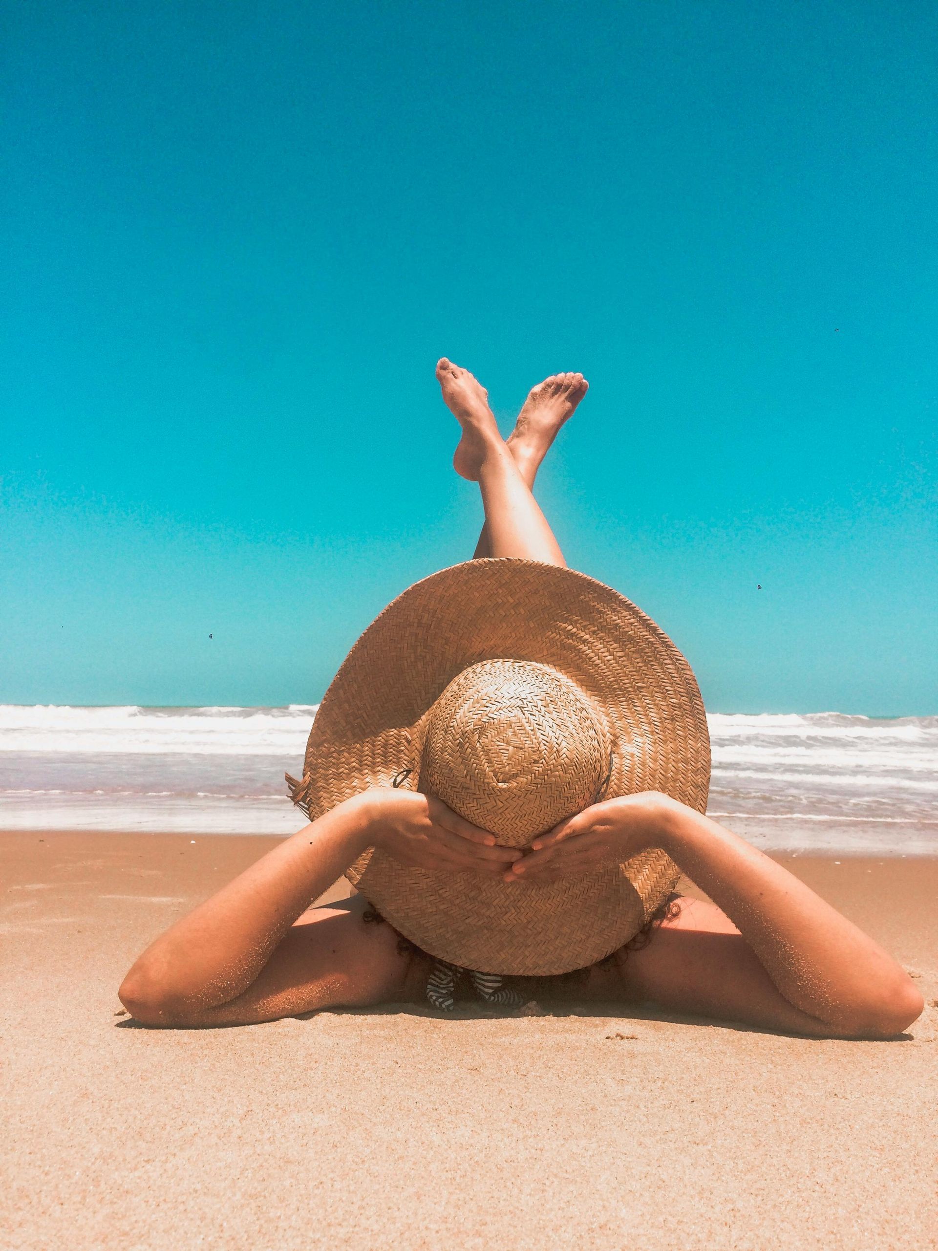 Eine Frau liegt mit einem Strohhut auf dem Bauch am Strand.