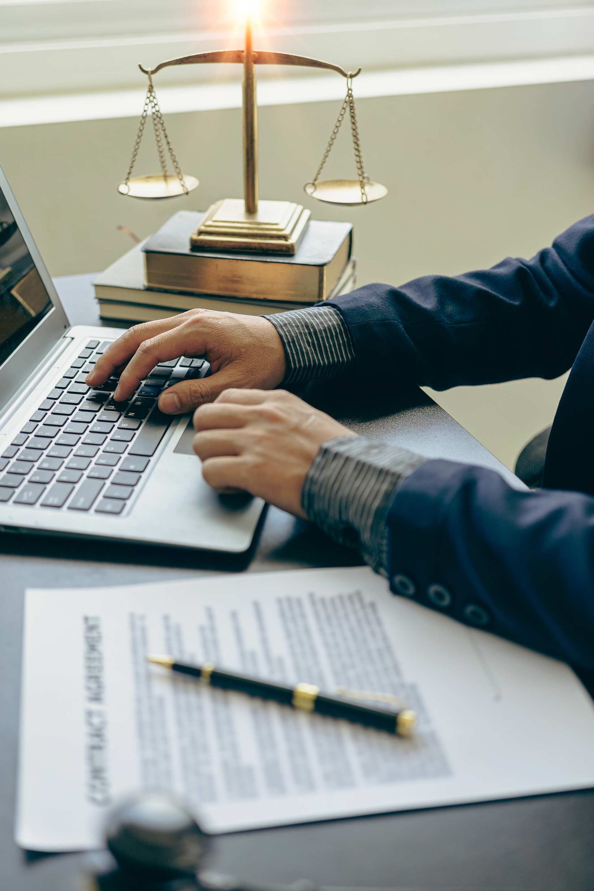 A man is typing on a laptop computer with a scale of justice in the background.