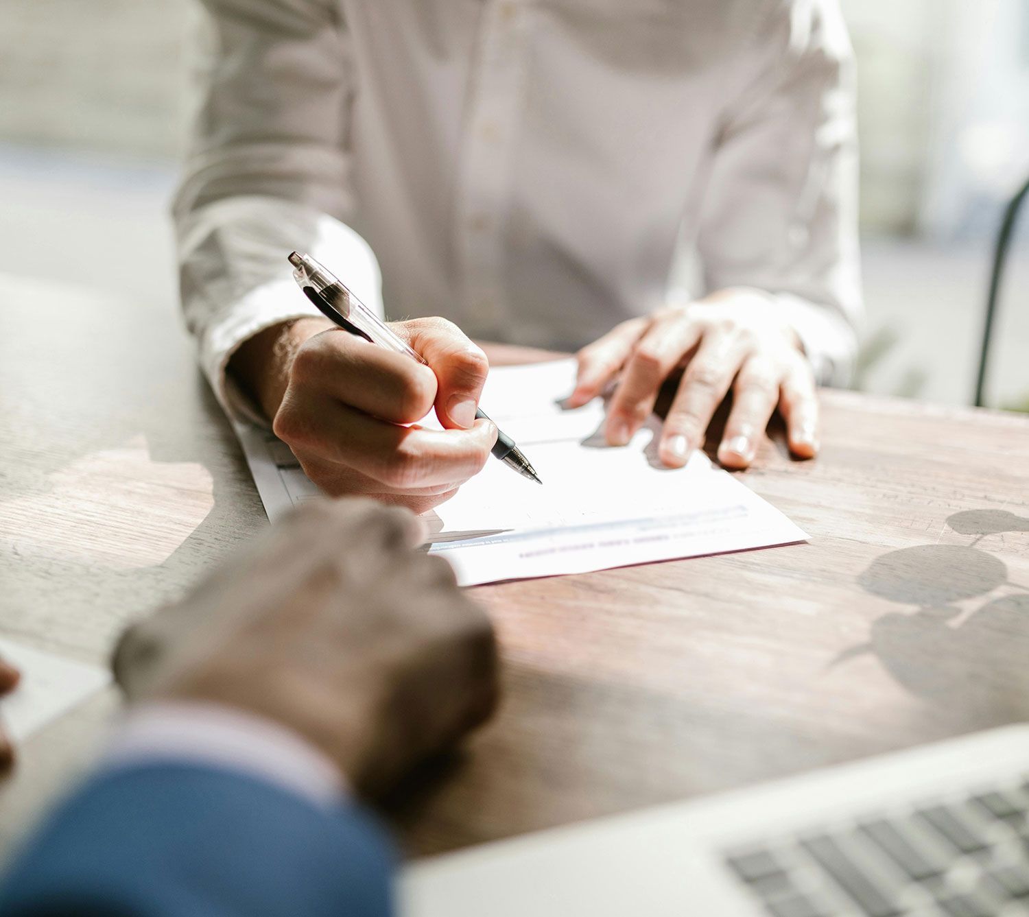 Two people signing a document at a desk, with a laptop in the foreground.