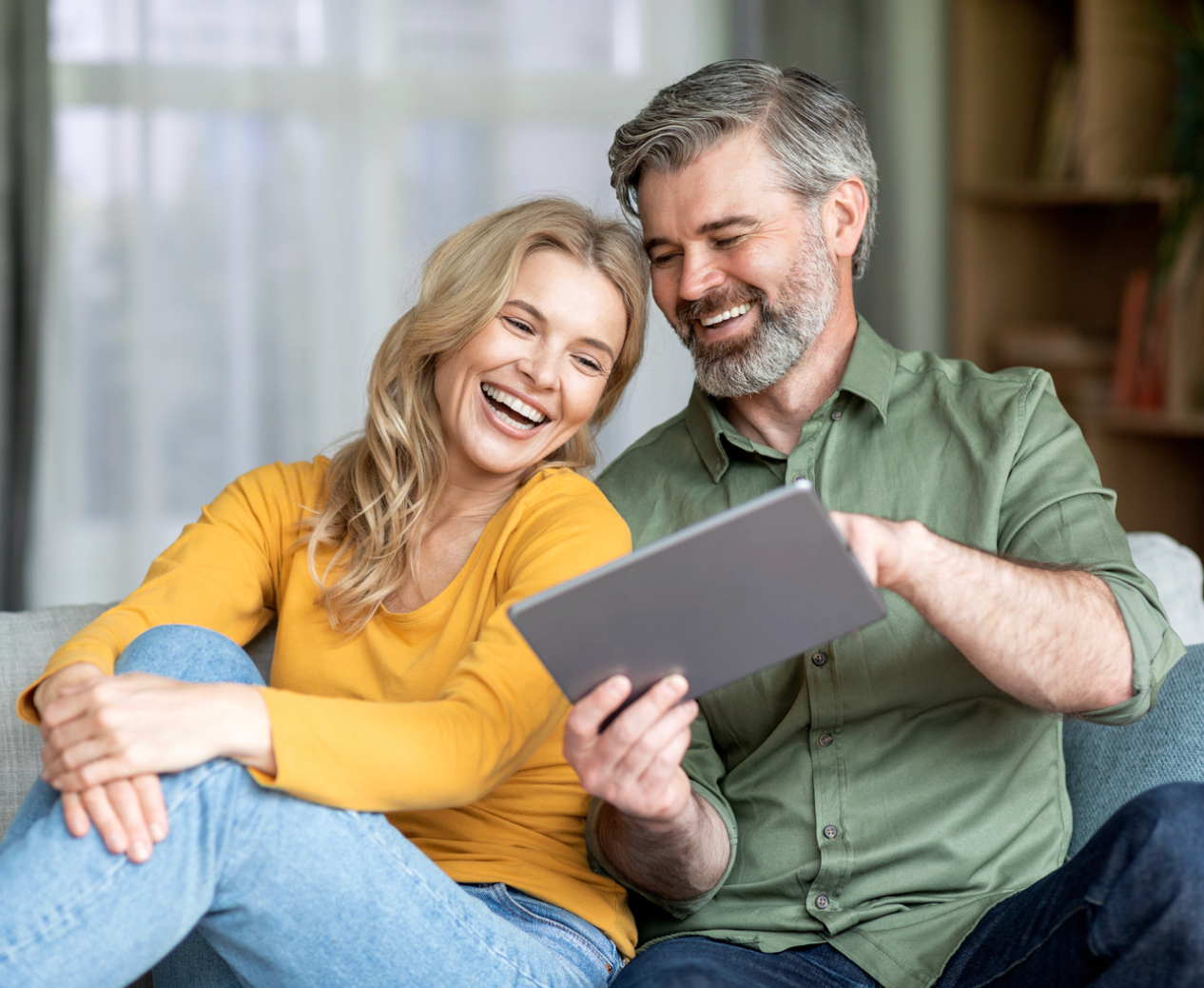 woman is a long-sleeve yellow tshirt sitting next to a man in a long-sleeve green button up tshirt holding a table smiling about reverse mortgage lenders near Cherry