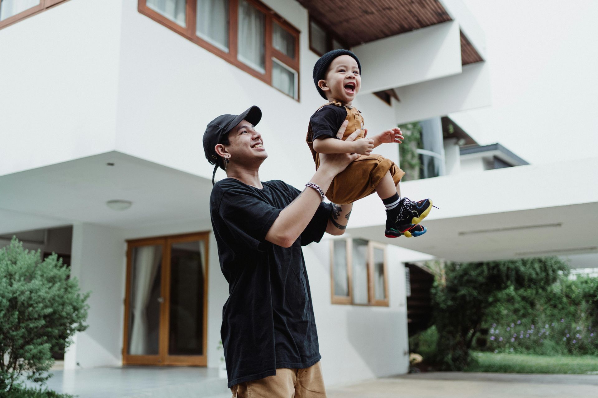 Man throws toddler in the air, both smiling. White house in background.
