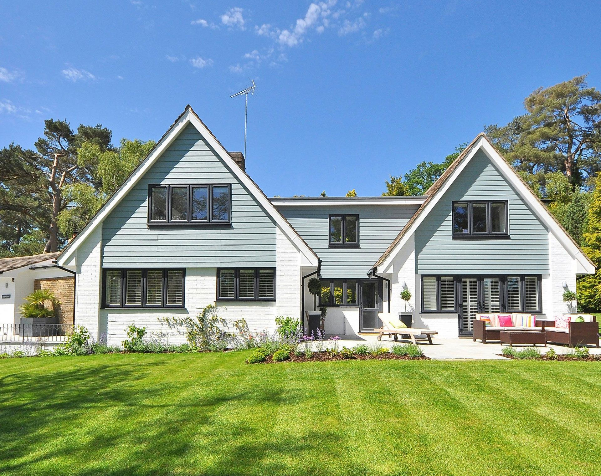 Large white and gray house with a manicured green lawn under a clear blue sky