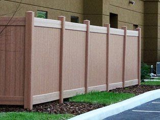 A wooden fence surrounds a parking lot in front of a building.