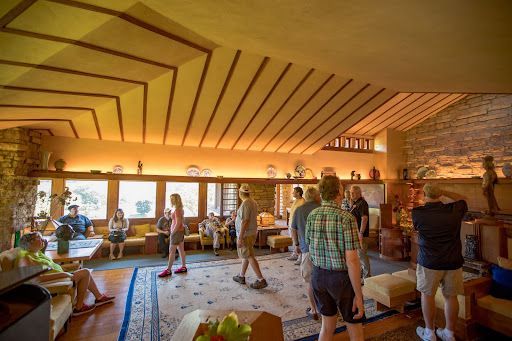 Interior of a building with people observing architecture. Beams, windows, and stone walls are visible.
