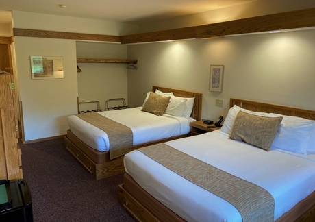 Hotel room with two queen beds, brown carpet, beige walls, and wood trim.