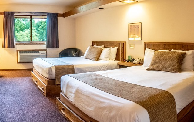 Hotel room with two double beds, window, air conditioner, and side table.