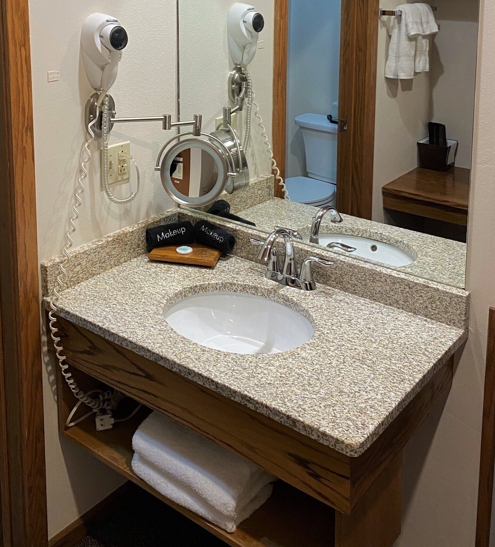 Bathroom vanity with a granite countertop, oval sink, mirror, and hairdryer.