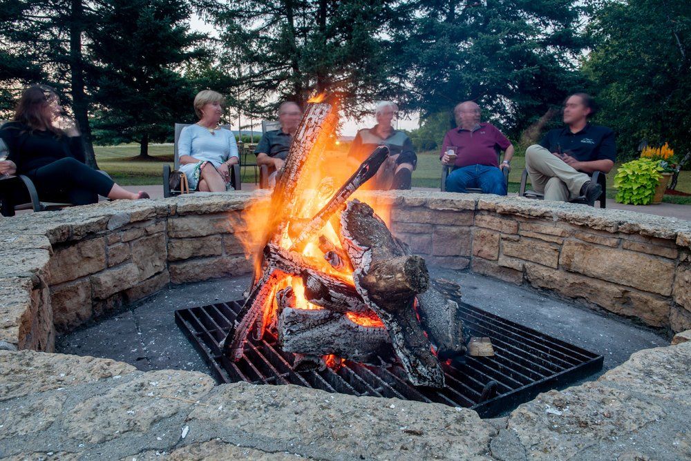 People around a fire pit with a blazing fire outdoors.