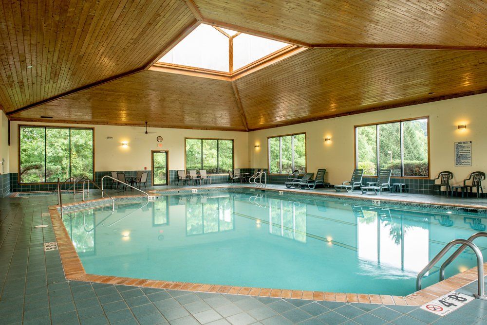 Indoor swimming pool with light blue water and large windows. Wooden ceiling.