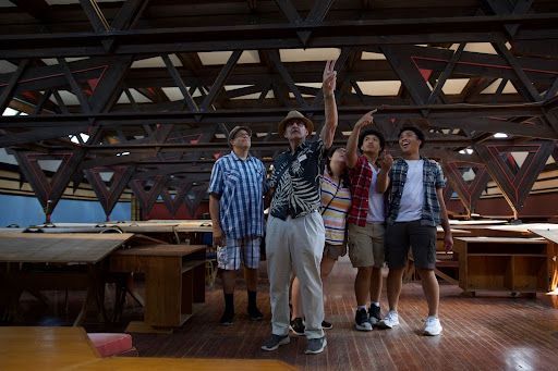 Man pointing up at ceiling, surrounded by four people in a large wooden structure.