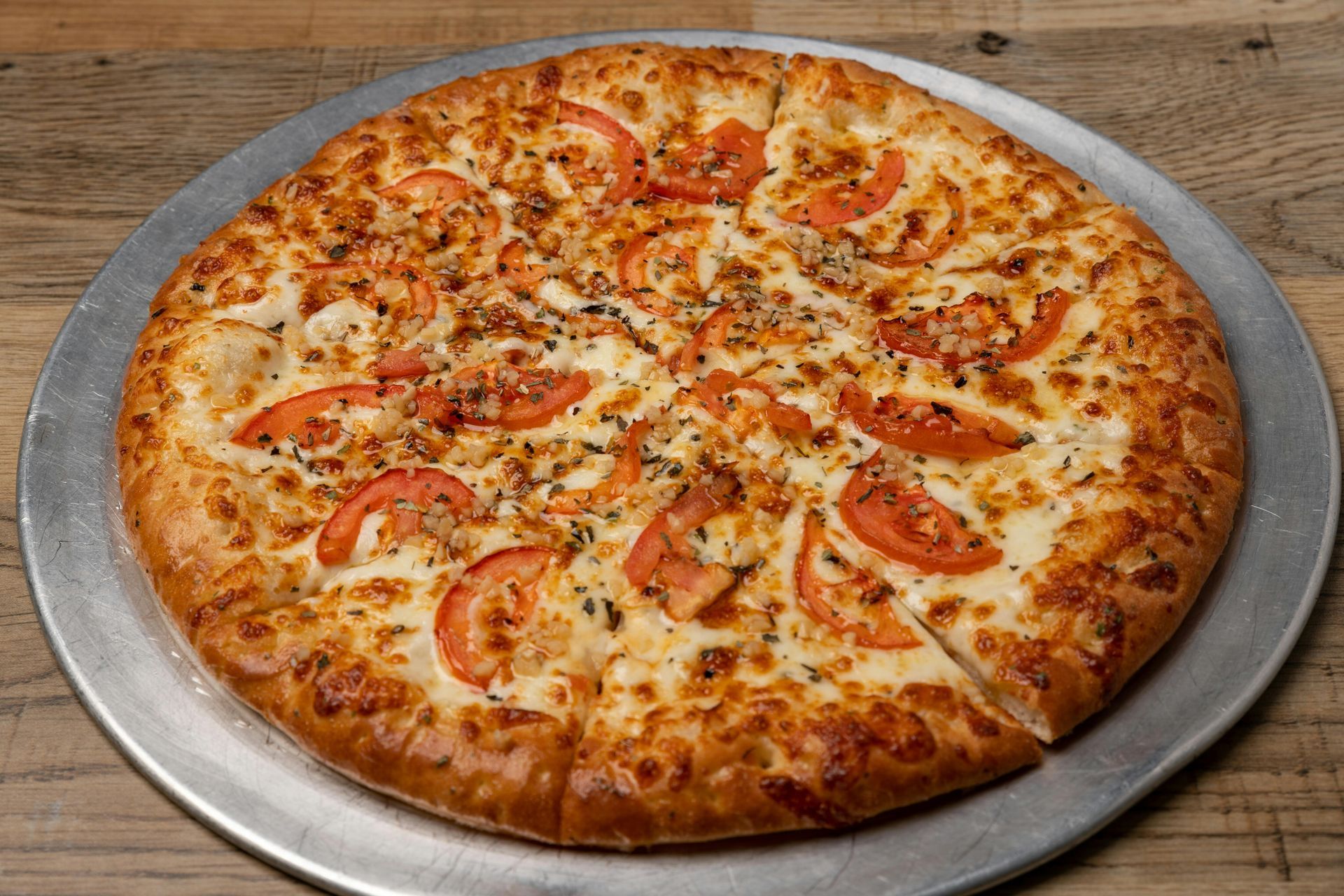 Pizza with tomatoes and cheese on a metal tray, cut into slices.