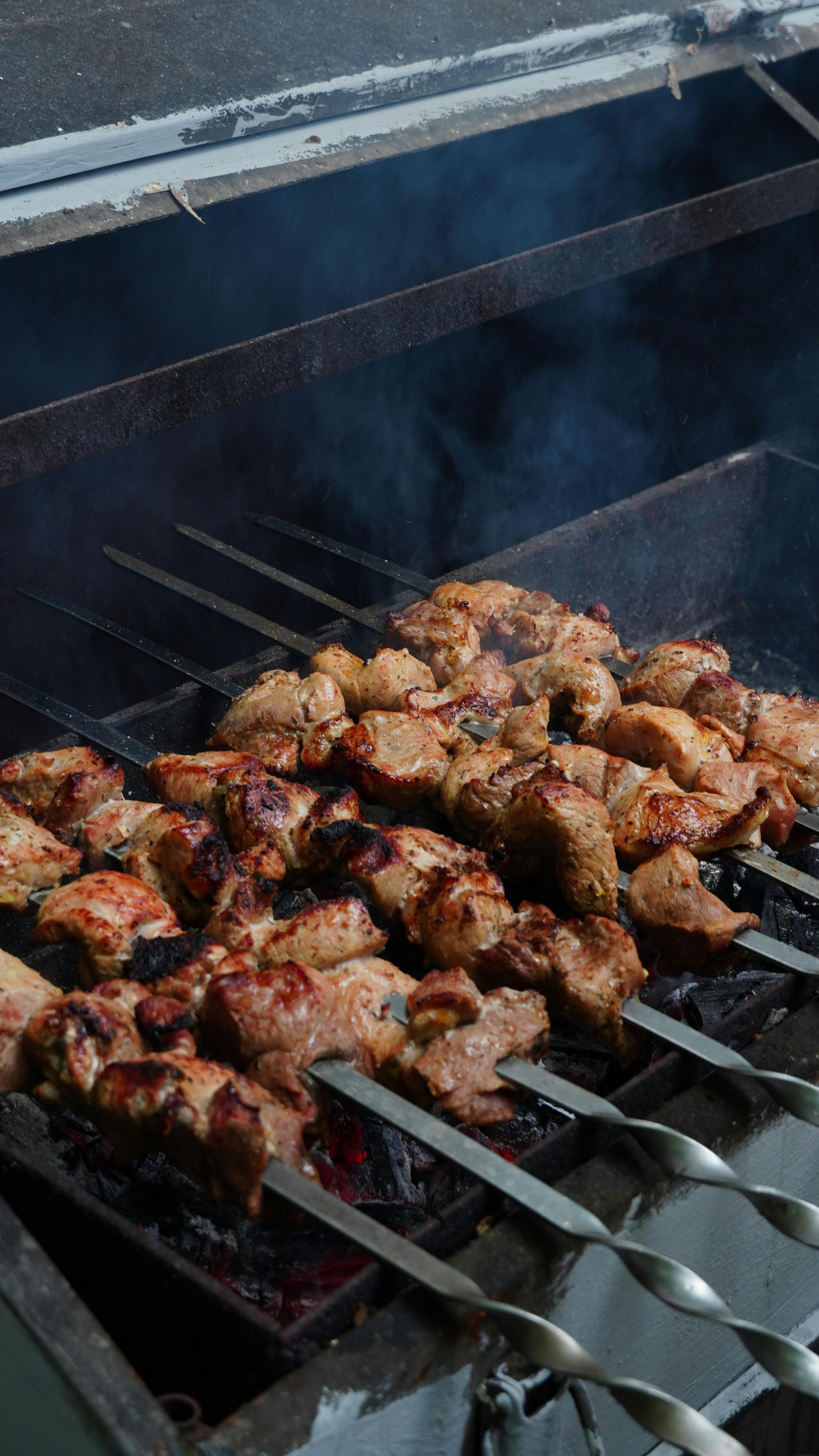 Meat skewers grilling on a barbecue, smoke rising.