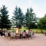 People seated around a fire pit on a patio, surrounded by trees.