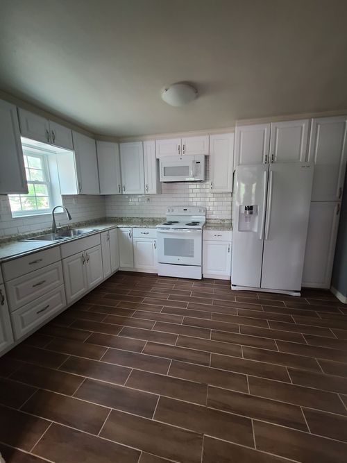 White kitchen with white cabinets, appliances, and brown tile flooring.
