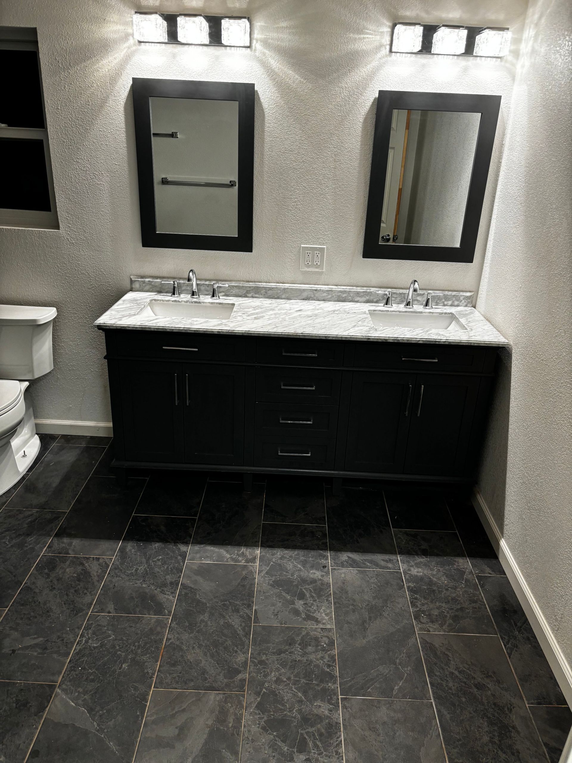 Bathroom with a black vanity, two mirrors, and dark tiled floor.