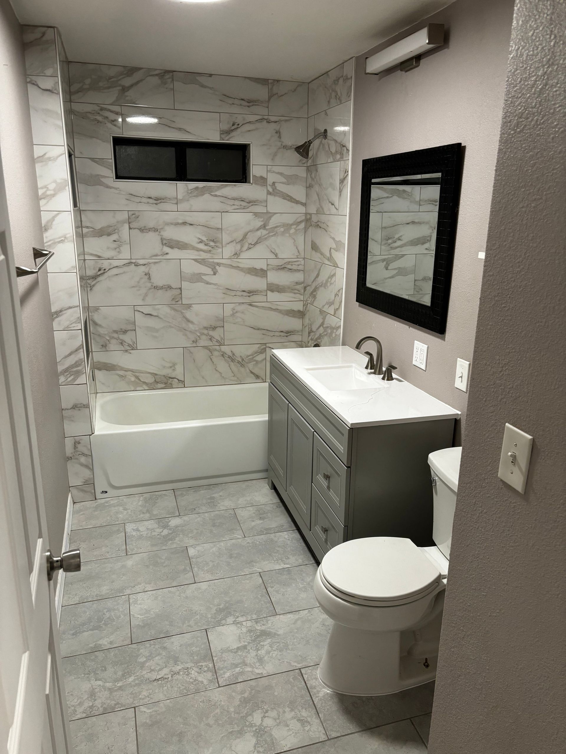 Bathroom with gray vanity, white toilet, tiled shower, and marble-like wall tile.