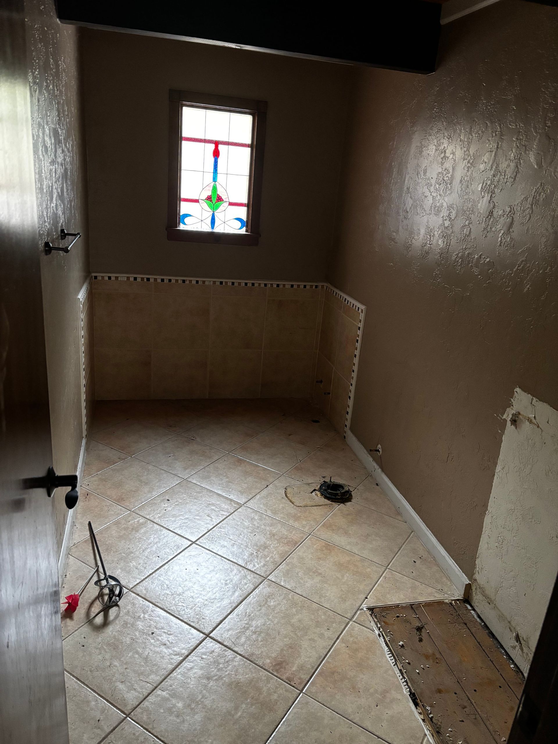Bathroom under renovation with partially tiled walls and floor. Stained glass window.