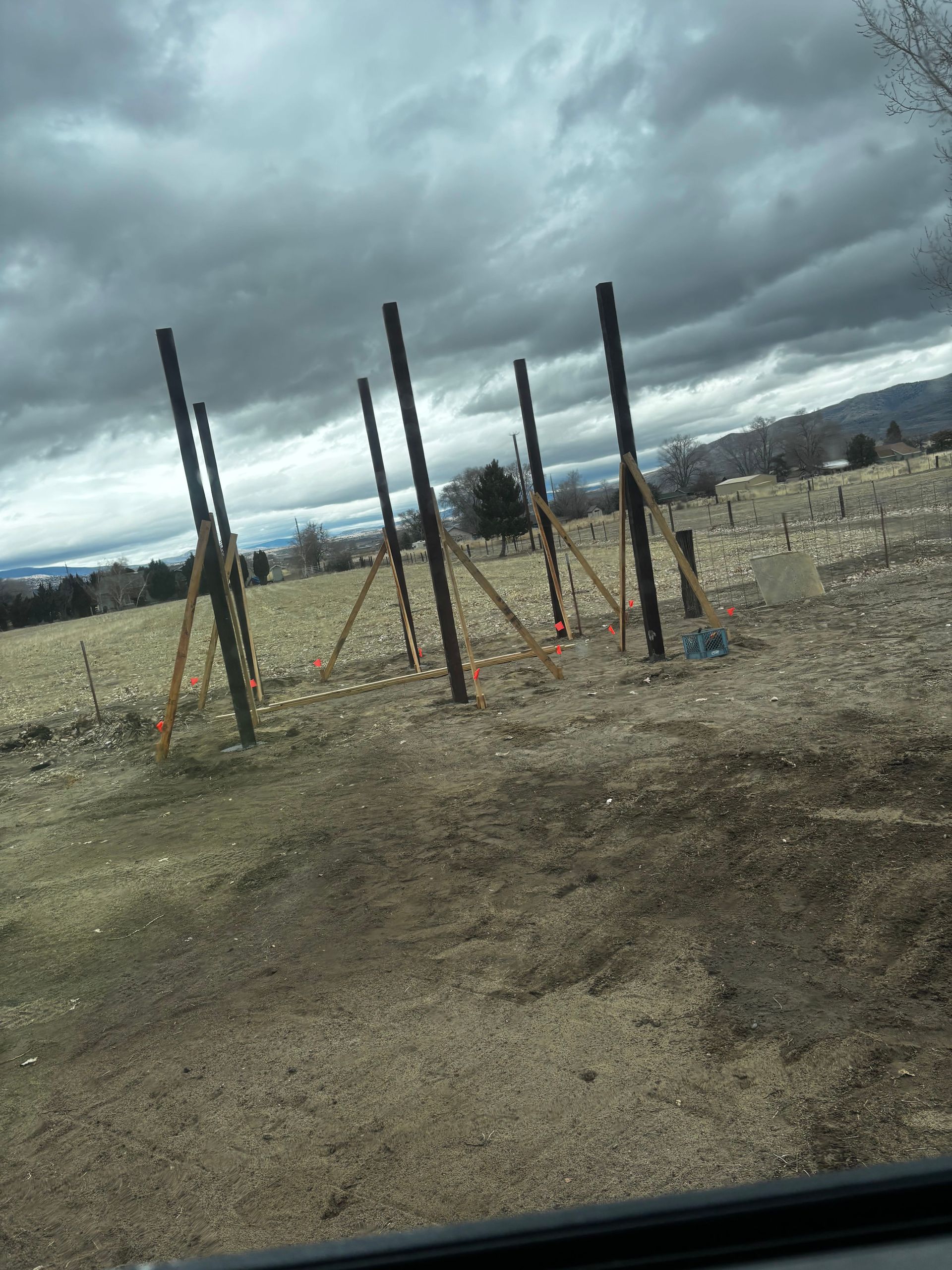 Wooden posts with support braces in a field under a cloudy sky.