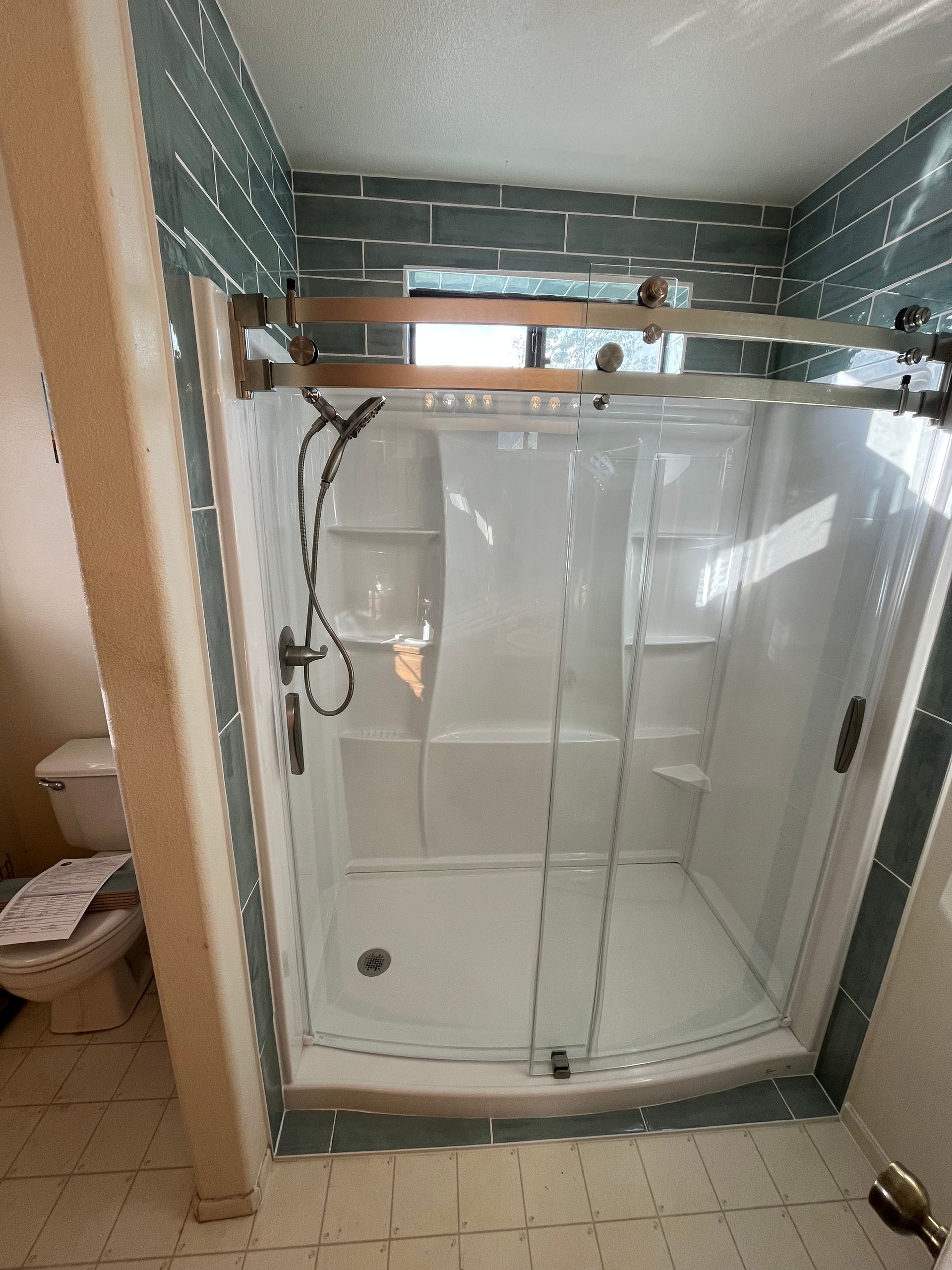 Bathroom with a white shower, glass door, and green tile backsplash.