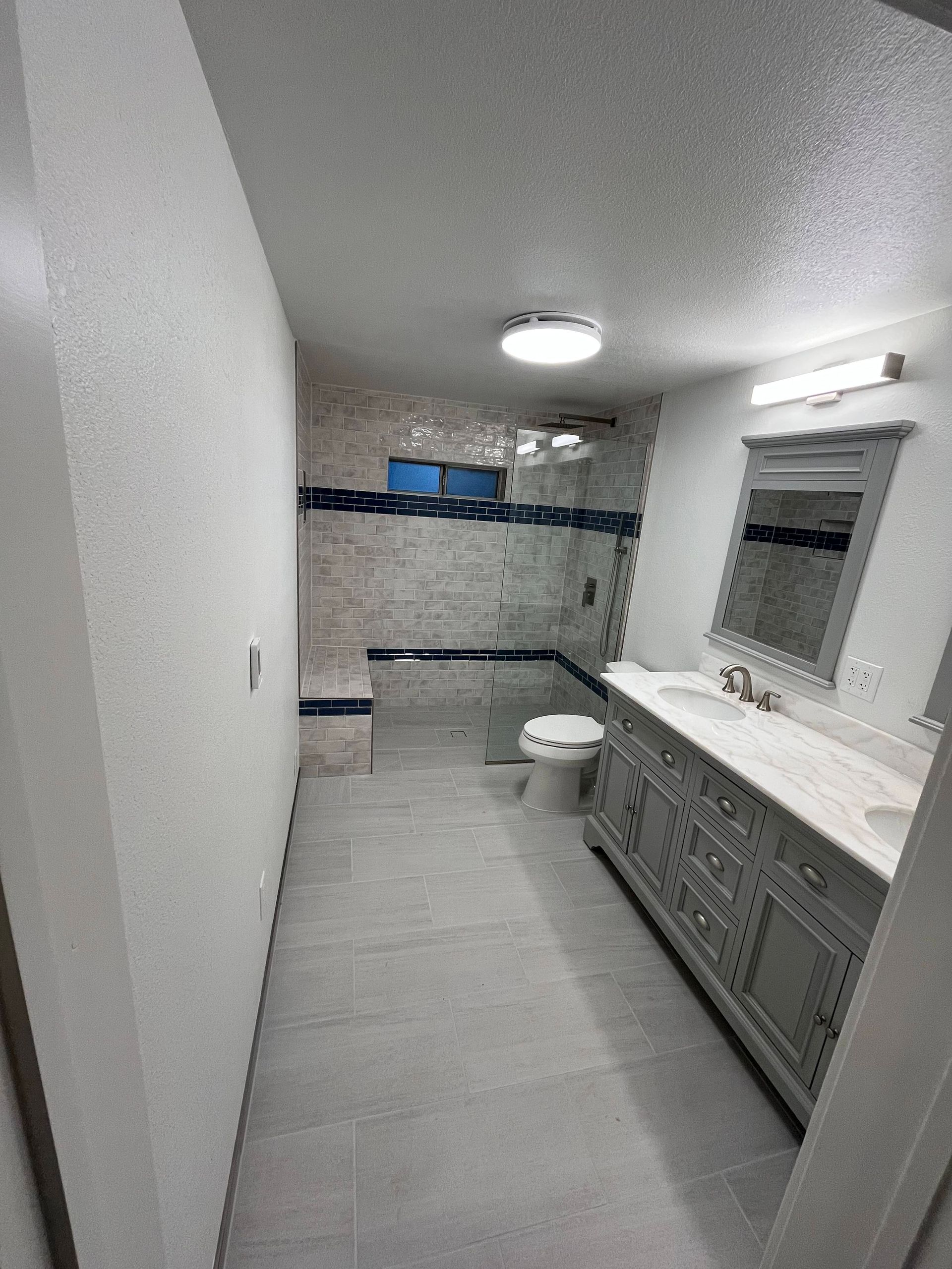 Bathroom with gray vanity, tiled shower with glass door, and large mirror.