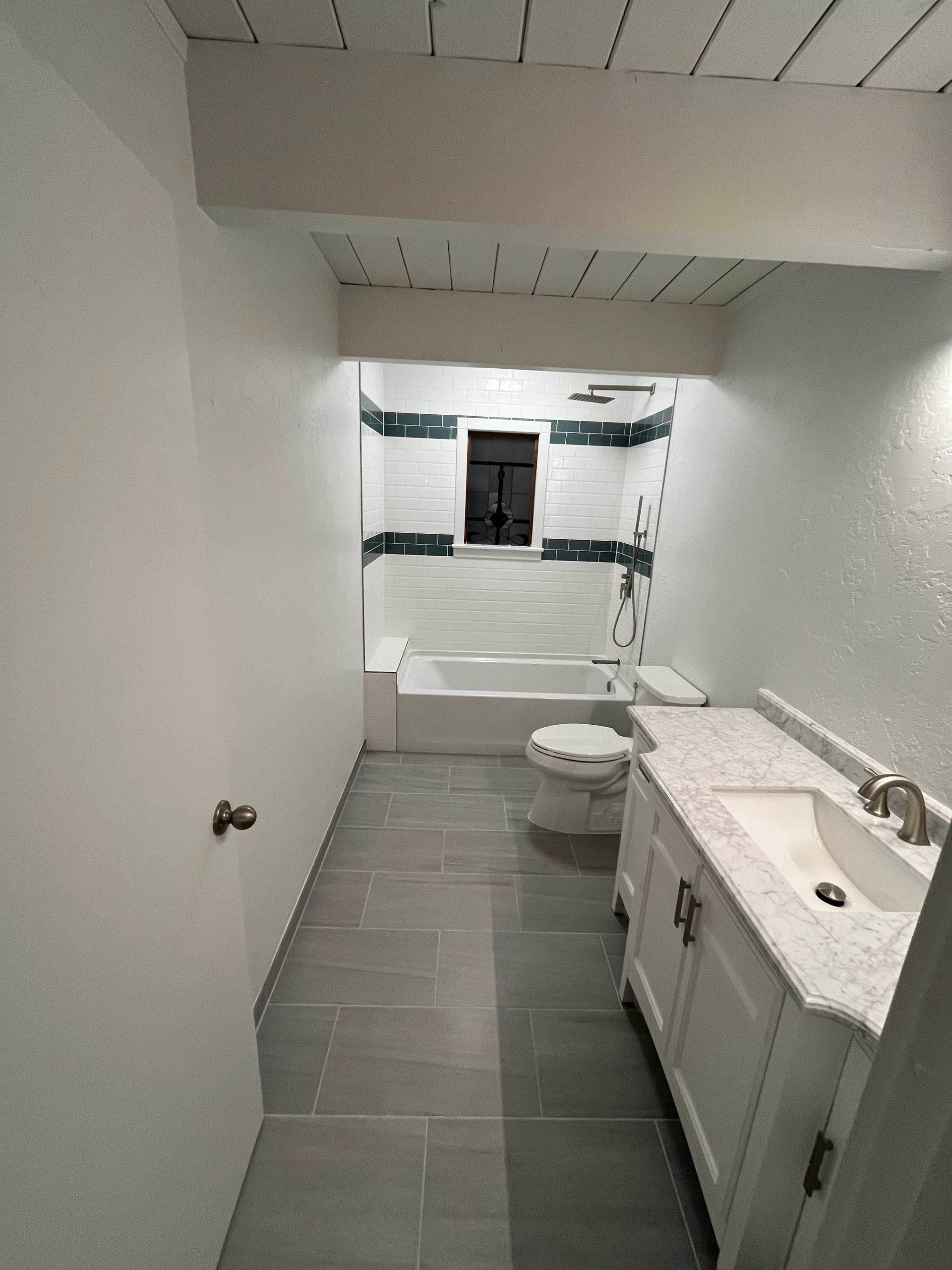 Bathroom with white walls, gray tile floor, white vanity, tub, and toilet. Blue and white tile accents.
