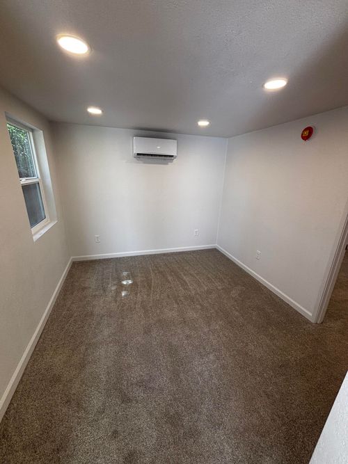 Empty room with carpet, air conditioner, small window, and recessed lights.