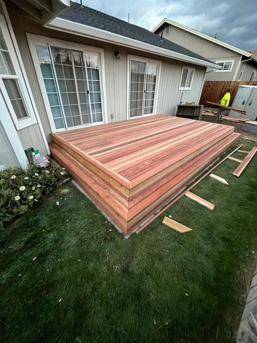 Newly built wooden deck on grass, near a house with sliding glass doors.