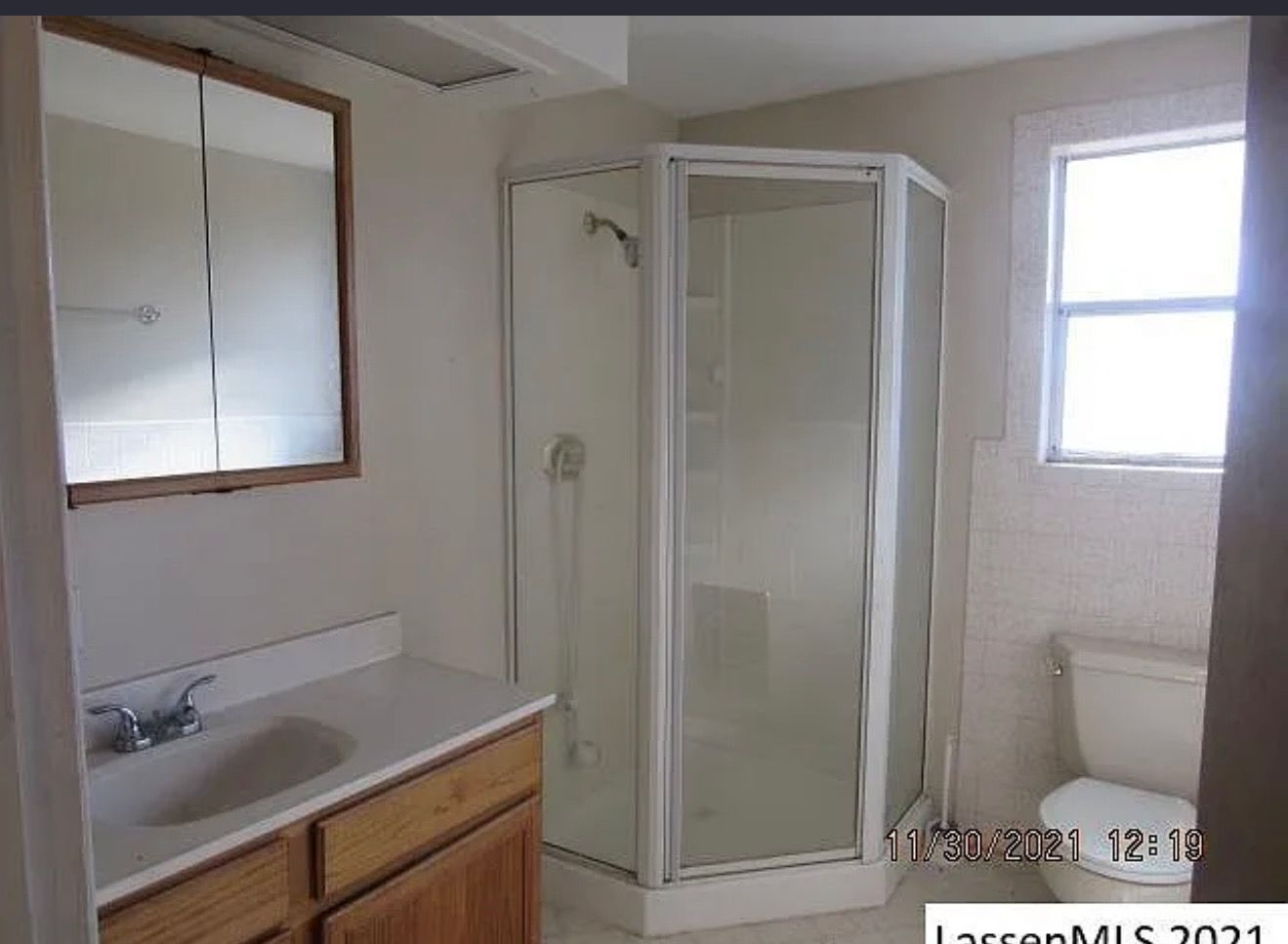 Bathroom with shower, vanity, toilet, and window. White shower enclosure, oak vanity.