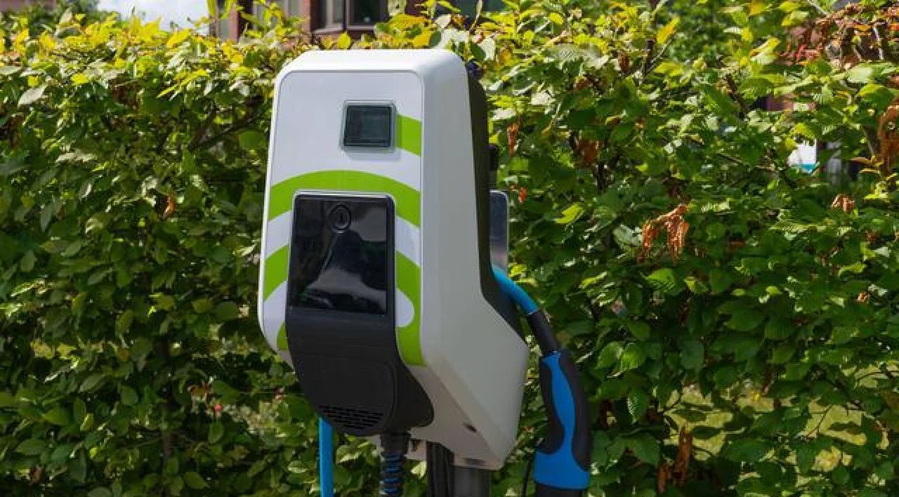 Electric vehicle charging station with green and blue cables in front of a hedge