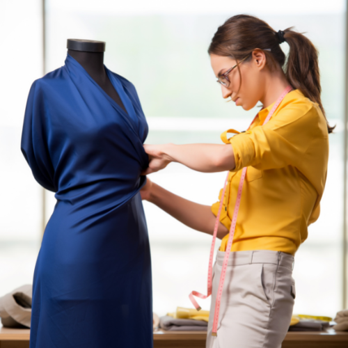 Fashion designer pinning blue fabric on a dress form while measuring with a yellow tape in a studio