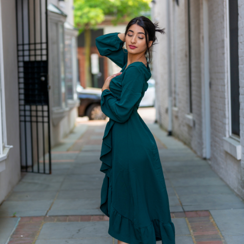Woman in a teal dress posing in a narrow alleyway with her hand behind her head.