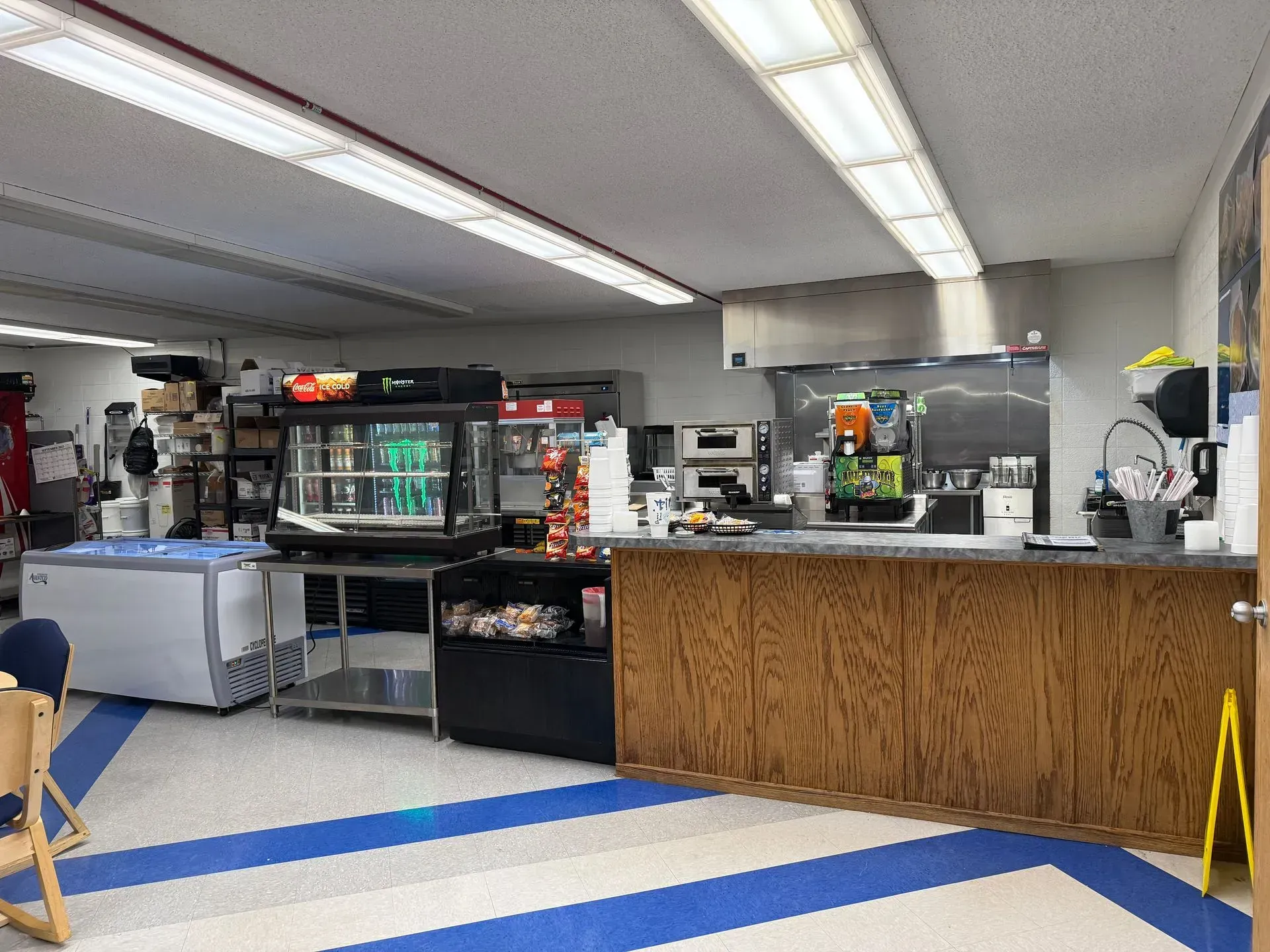 Two people smiling behind a deli counter with food and utensils in a kitchen or café