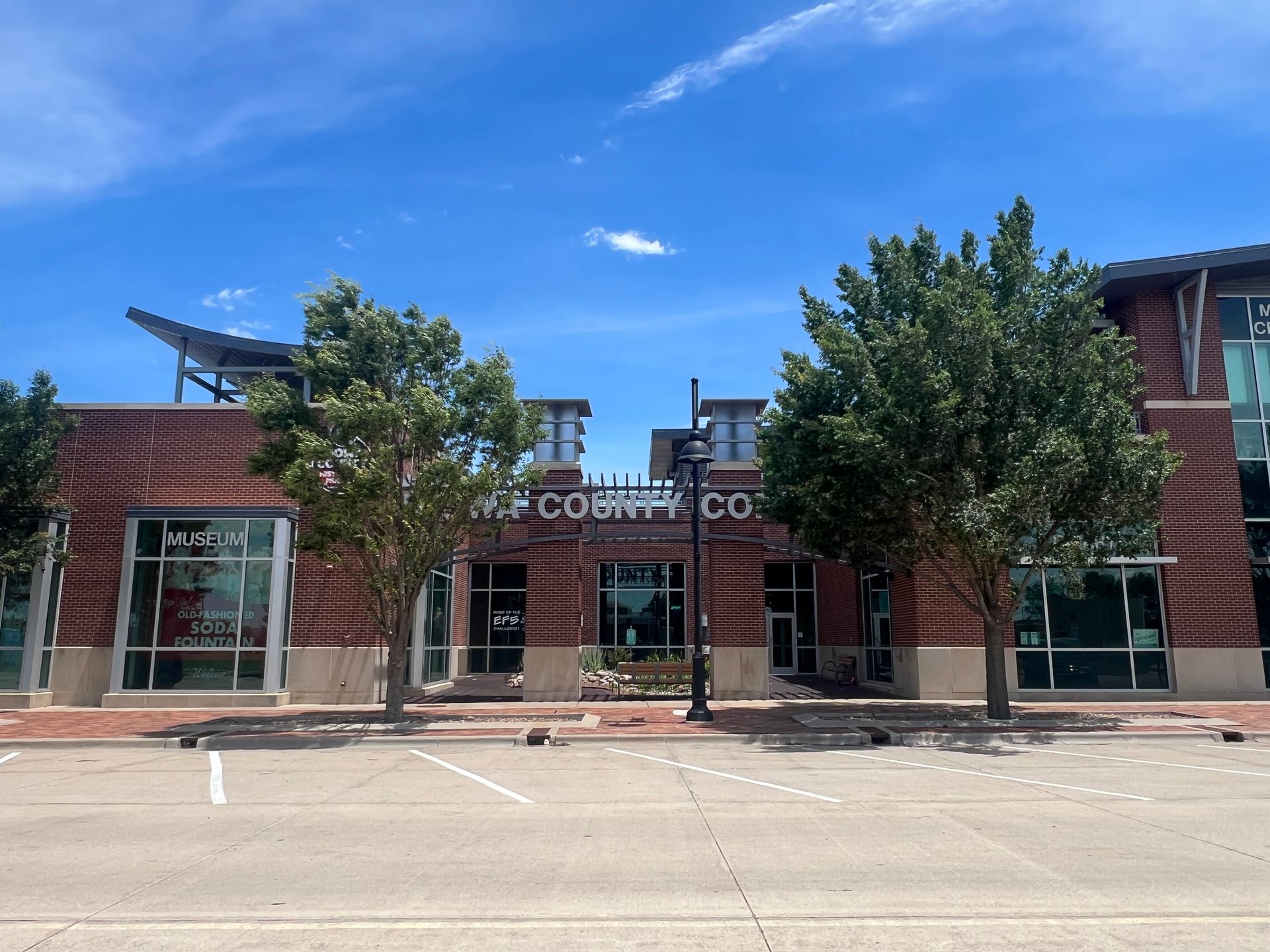 Brick storefronts with large windows and trees under a clear blue sky, including a coffee shop entrance.