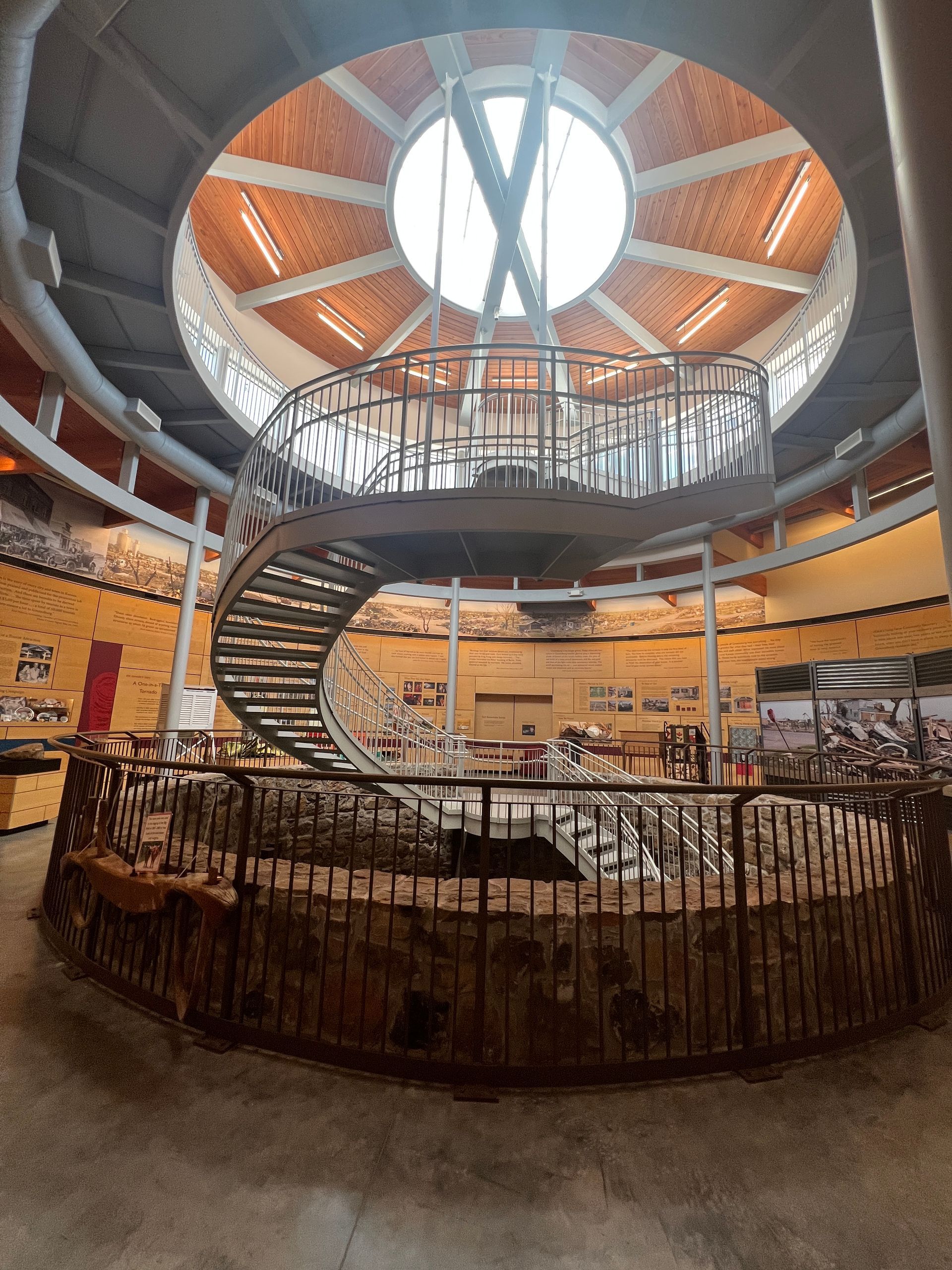 Circular museum atrium with spiral staircase, central sculpture, and skylight above a seating area