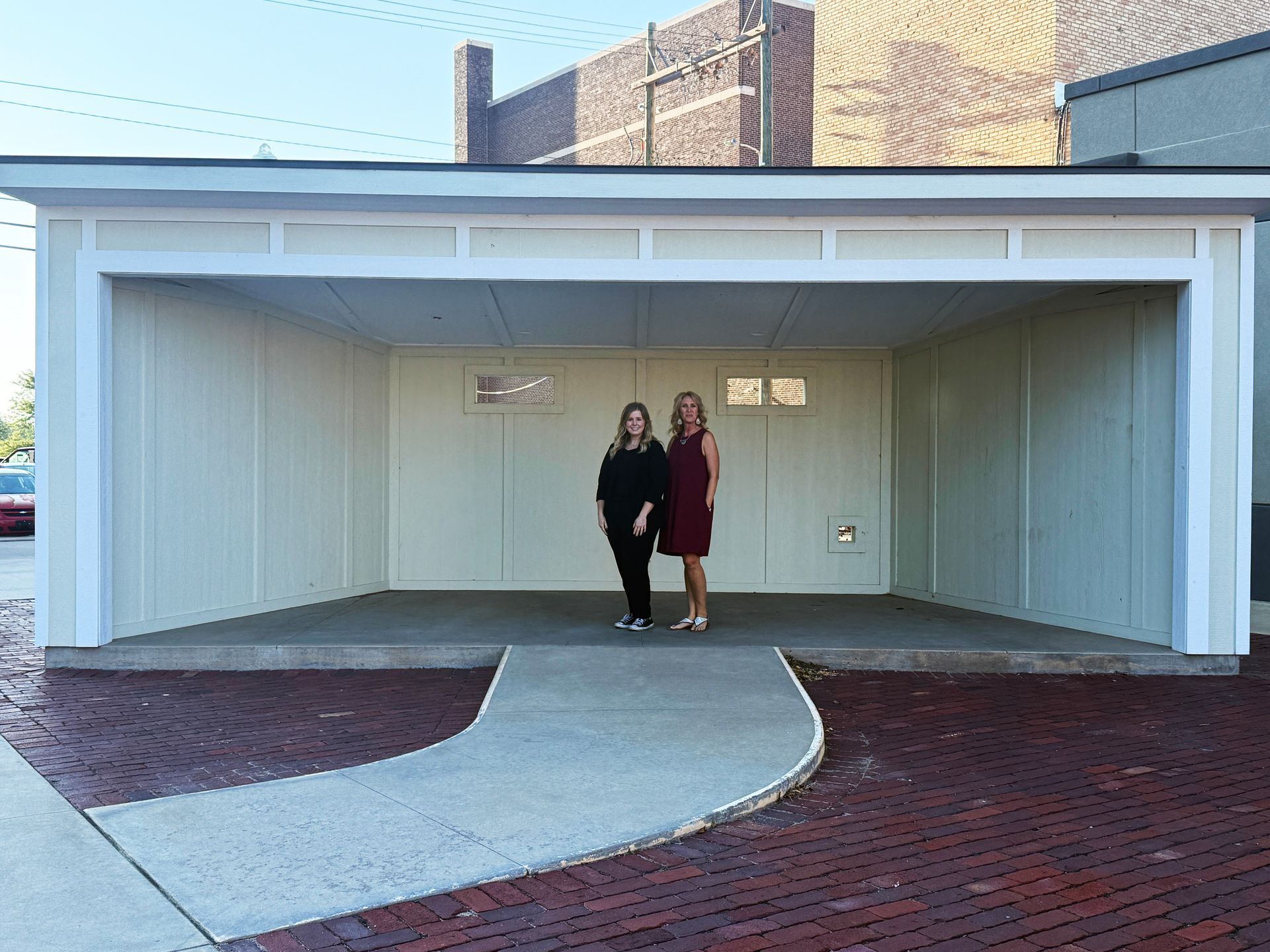 Two people standing in a white covered driveway beside a brick building.